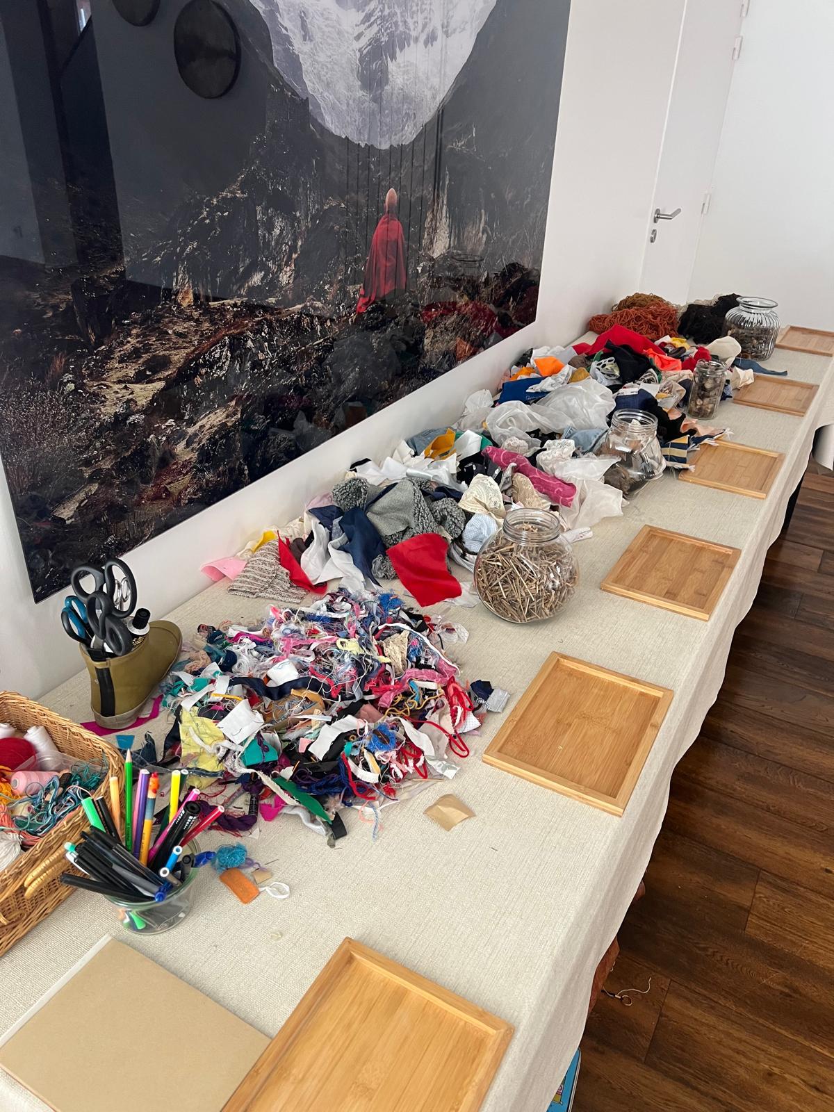 Table d'atelier dressée pour une séance couples : tissus colorés, rubans, ciseaux, feutres et planches individuelles en bois
