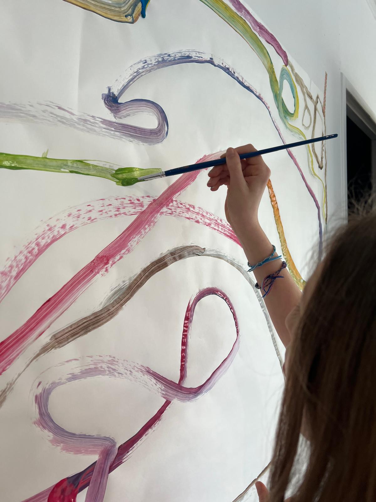 Main d'une enfant traçant de grands gestes de peinture colorés sur une feuille murale en atelier d'art-thérapie