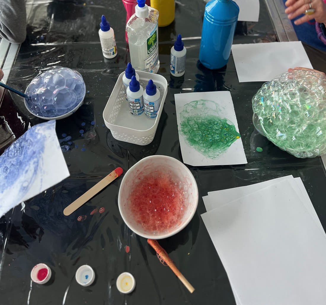 Atelier bulles : bols de peinture mousseuse colorée, flacons et empreintes de bulles sur papier