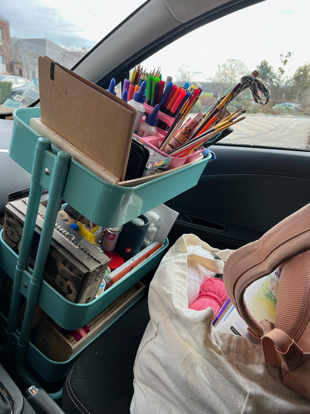 Chariot d'art-thérapie chargé de crayons, feutres, pinceaux et carnets, installé dans une voiture