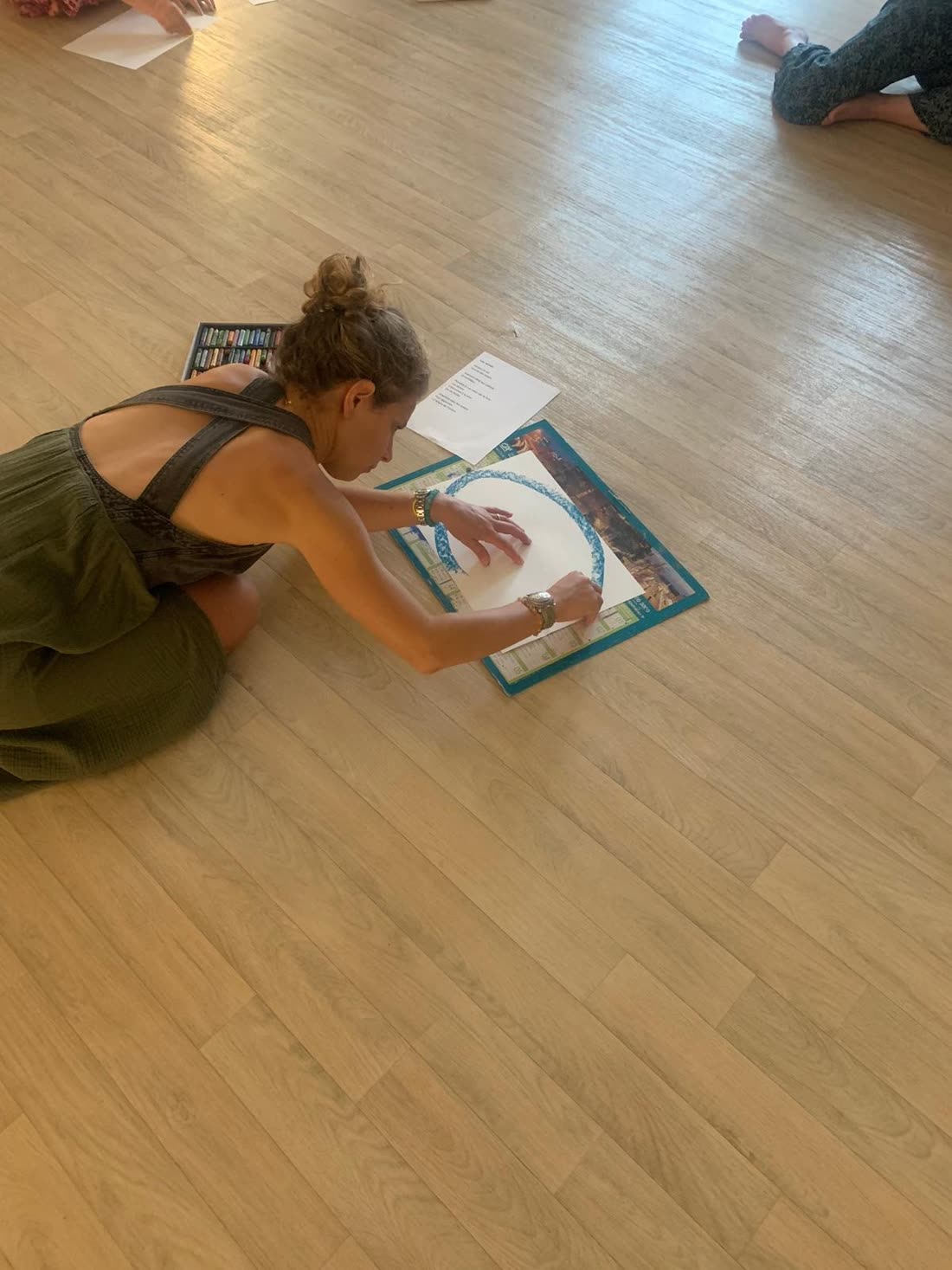 Raphaëlle allongée au sol, traçant un cercle au pastel sur une grande feuille
