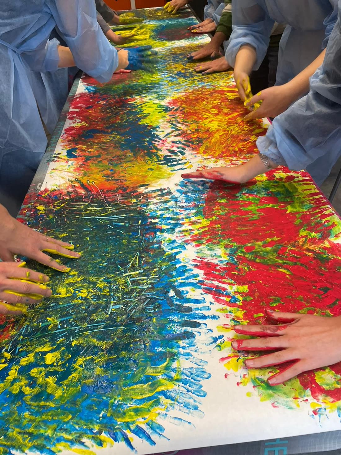 Fresque collective peinte à mains nues, traces rouges, bleues et jaunes sur un long rouleau de papier