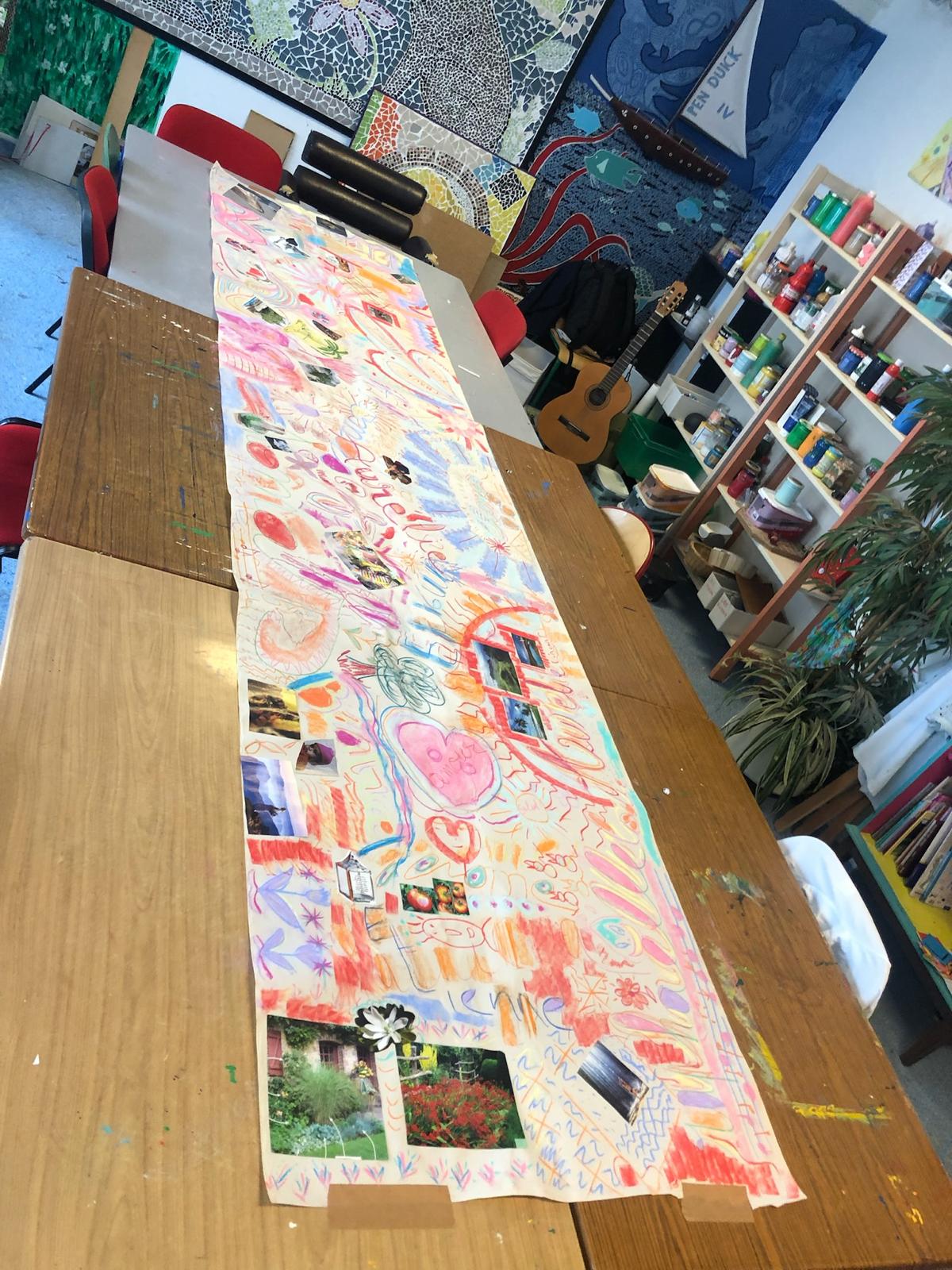 Grande fresque collective colorée étalée sur une table dans un atelier d'art-thérapie, réalisée à l'hôpital de jour de Dieppe