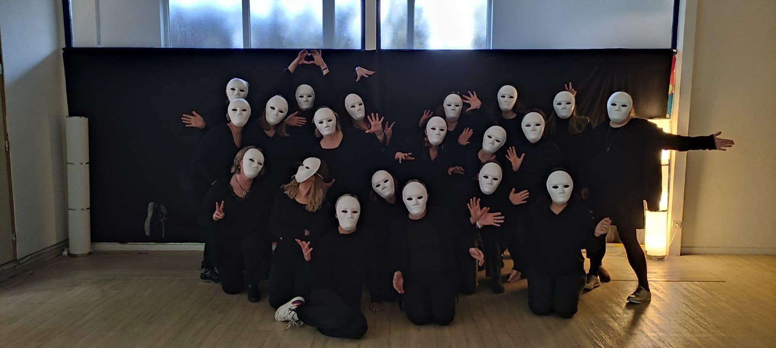 Groupe vêtu de noir portant des masques blancs neutres, mains ouvertes et expressives