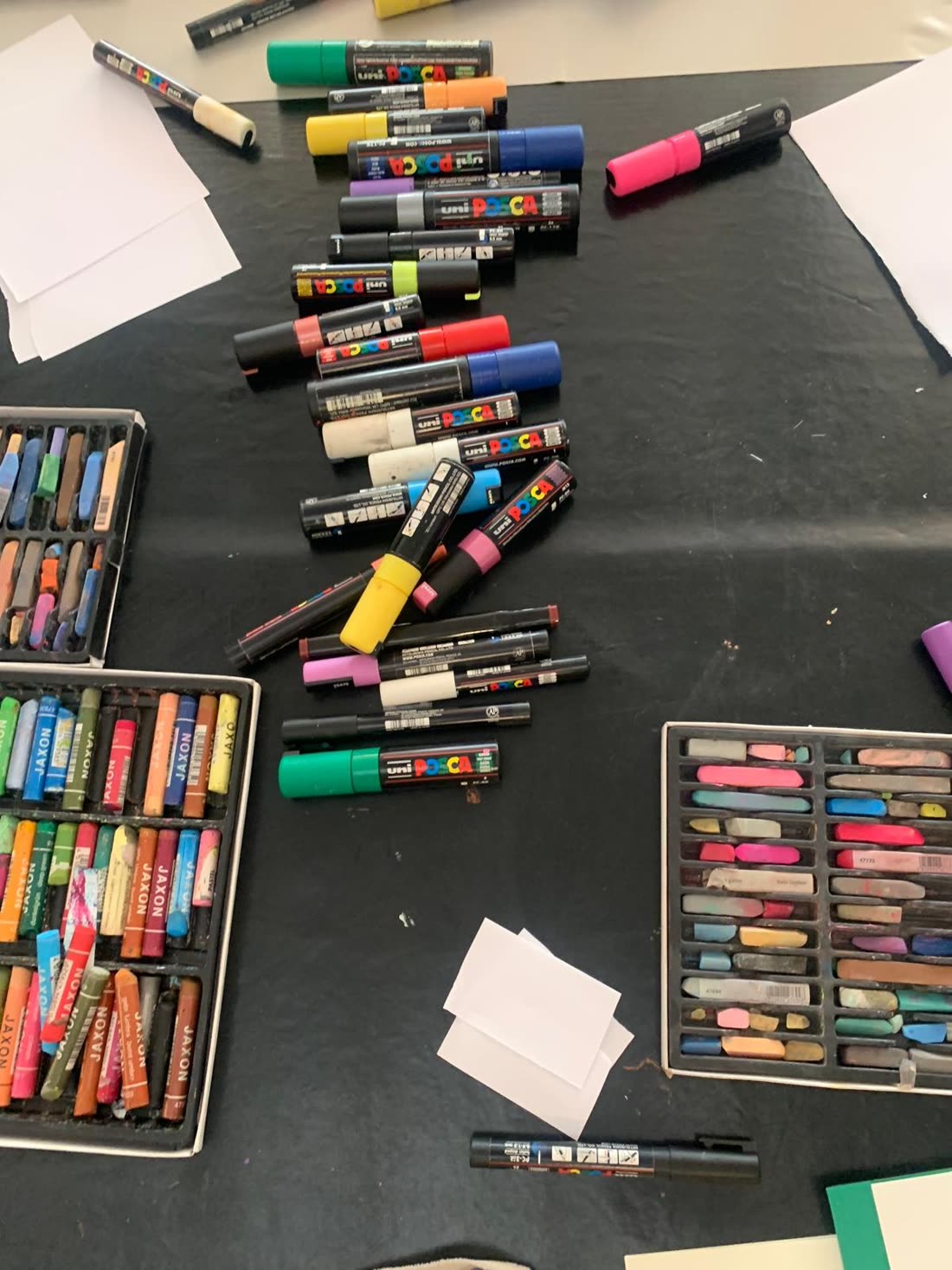 Feutres Posca de toutes les couleurs et coffrets de pastels secs disposés sur une table noire