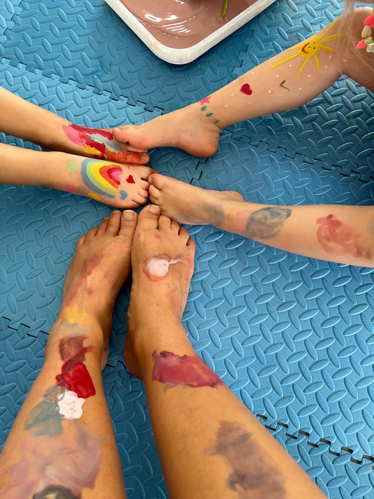 Pieds et jambes d'enfants recouverts de peinture colorée — arc-en-ciel, soleil, cœurs — sur un tapis bleu d'atelier