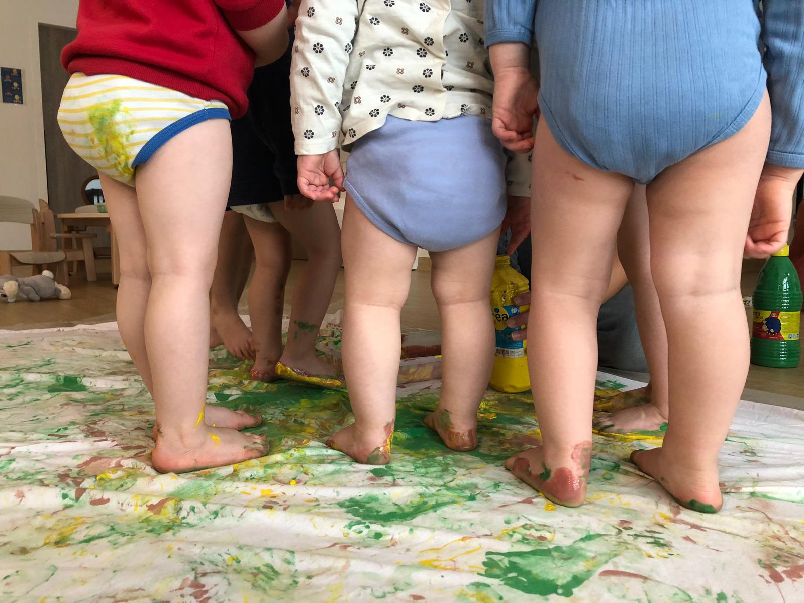 Petits pieds de tout-petits barbouillés de peinture verte et jaune, debout sur une grande feuille colorée en atelier d'éveil